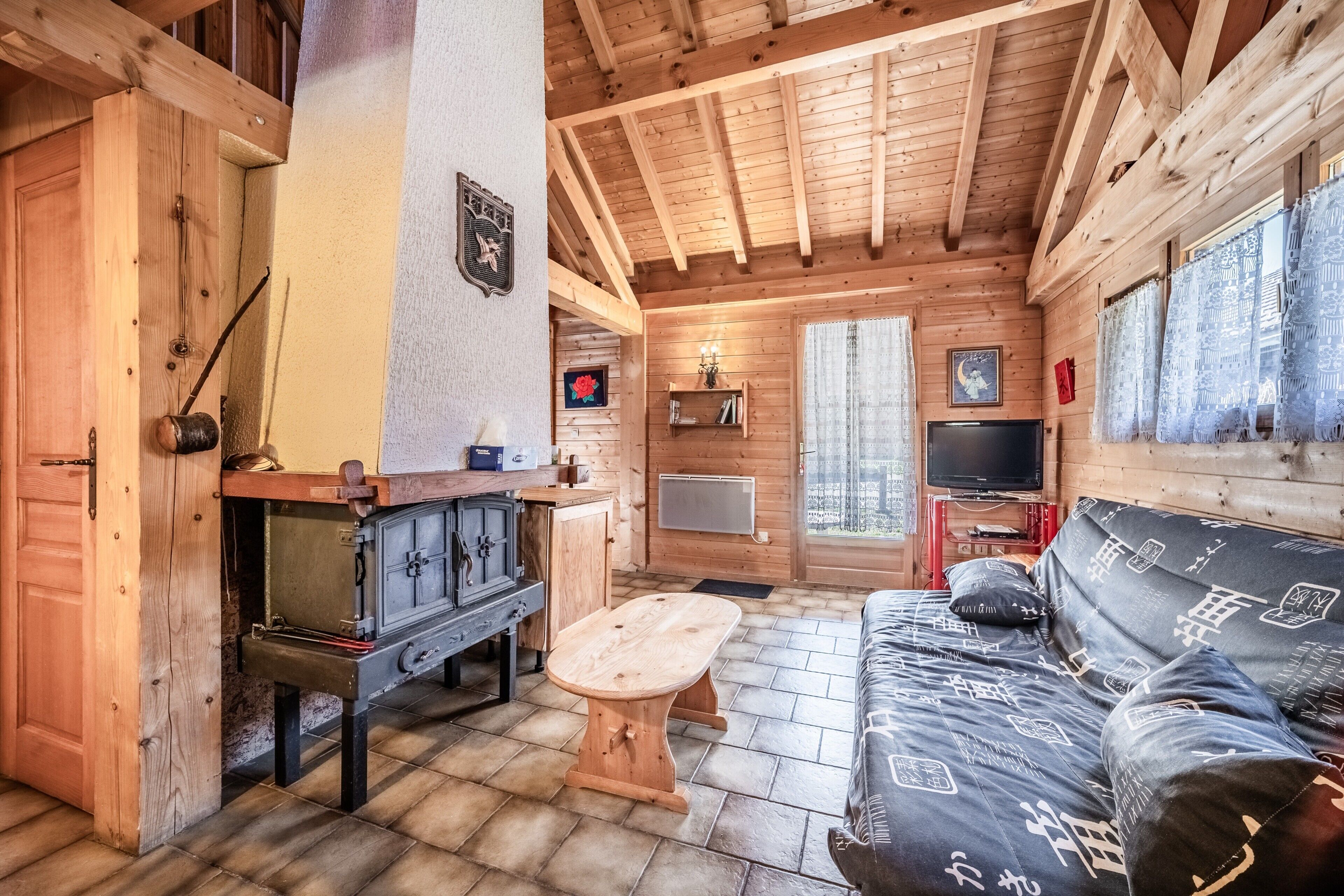 Interior de una cabaña de madera con sofá, una mesa, chimenea y televisor.