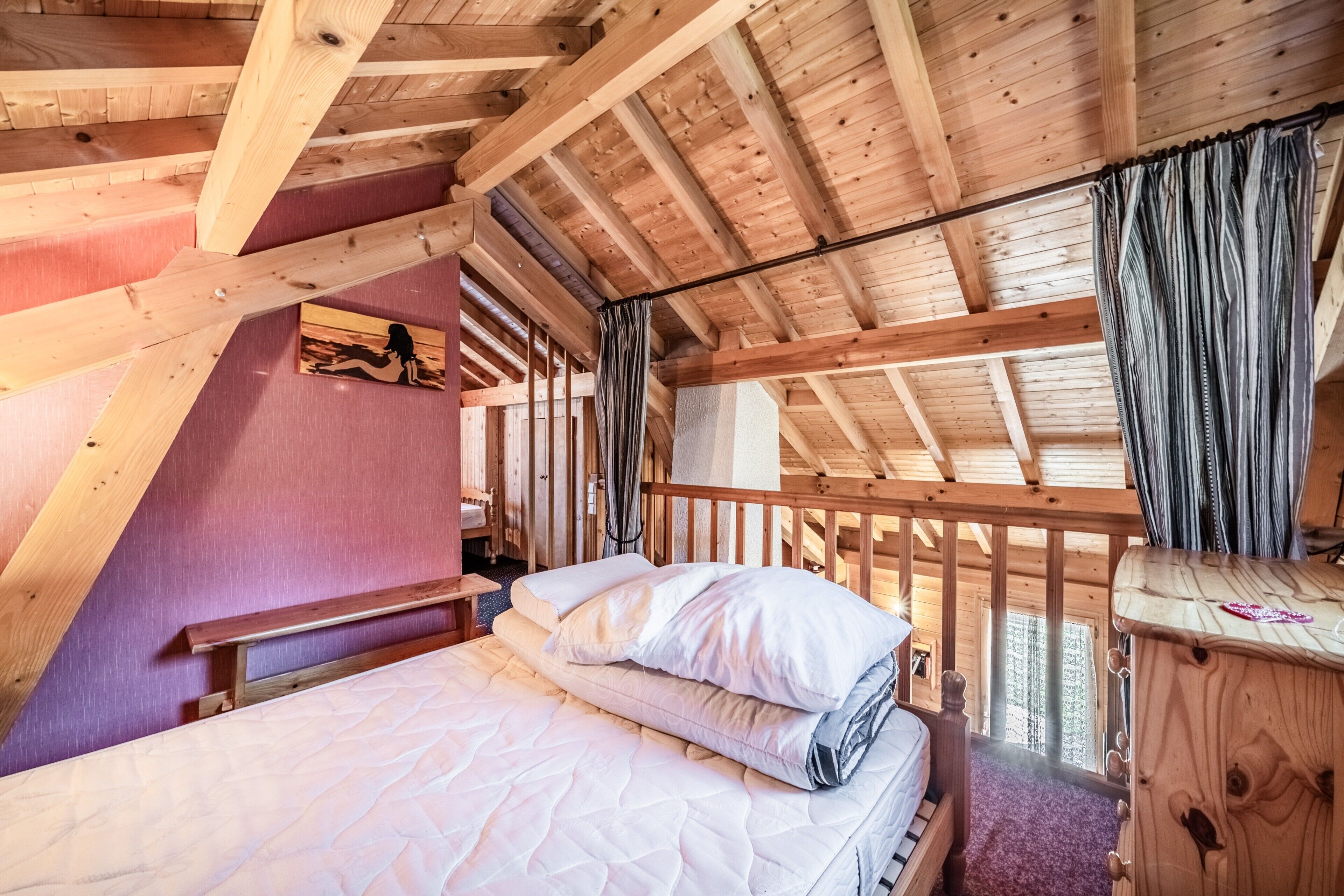 Una habitación tipo cabaña de madera con una cama, una ventana con cortinas y techo de madera.