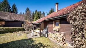 En træhytte med rødt tegltag, en overdækket veranda og et lille udendørs siddeområde.