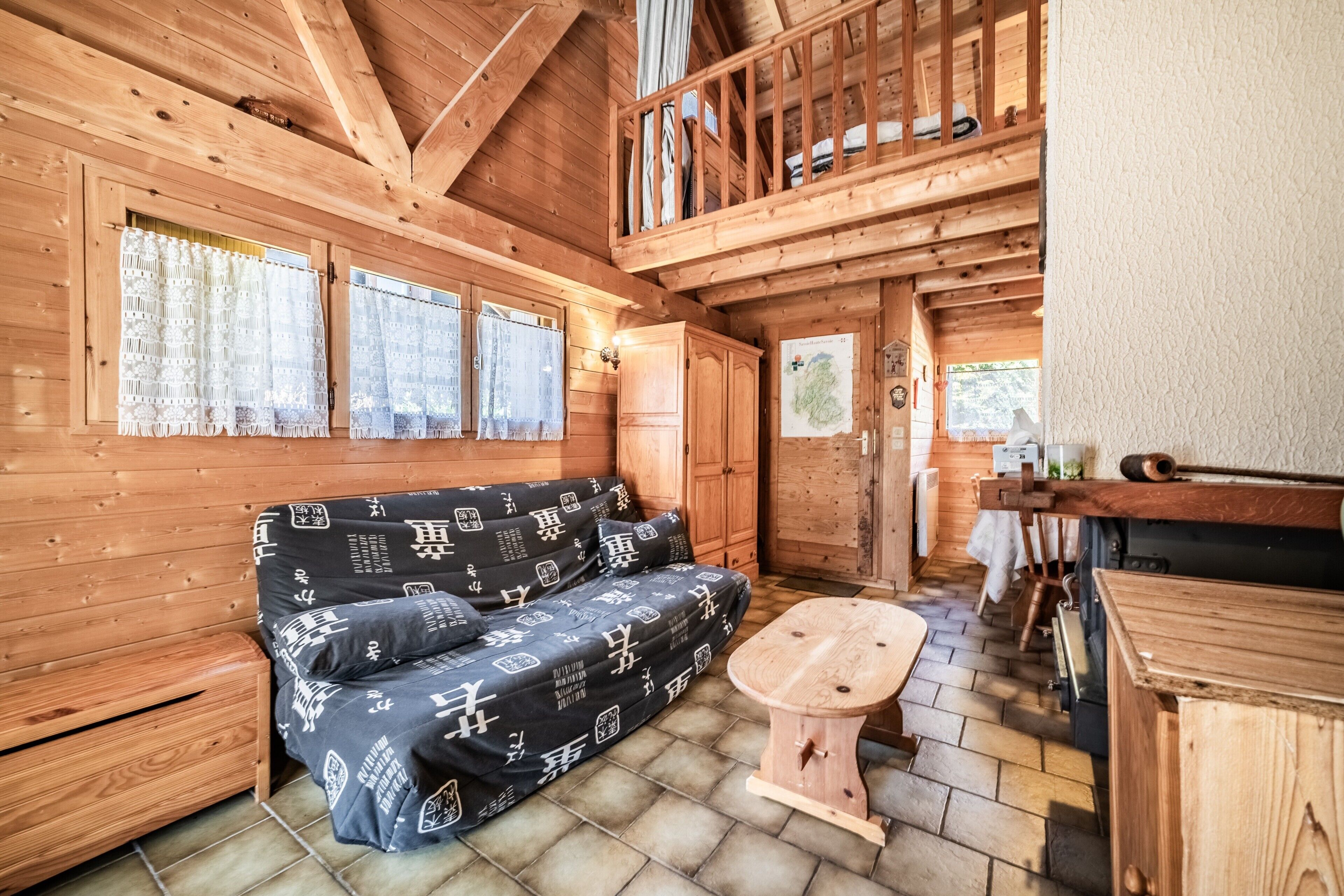 Interior de una cabaña de madera con un sofá, una mesita de madera y un altillo.
