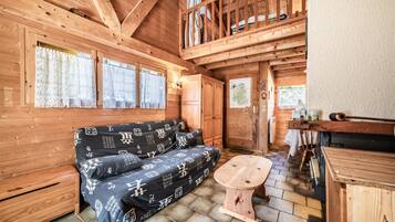 Interior de una cabaña de madera con un sofá, una mesita de madera y un altillo.