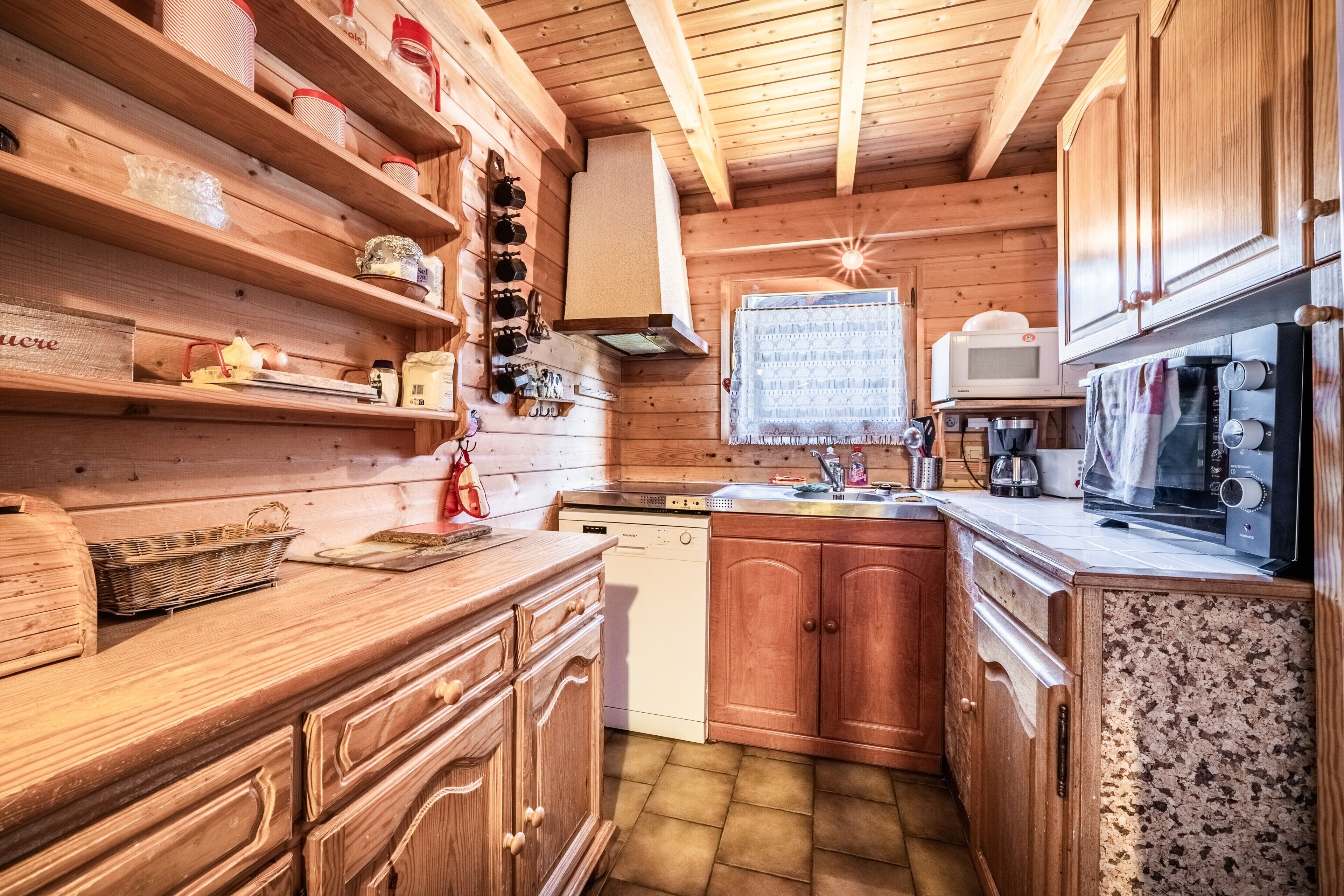 Interior de una cabaña de madera con área de cocina, armarios de madera, microondas y lavavajillas.