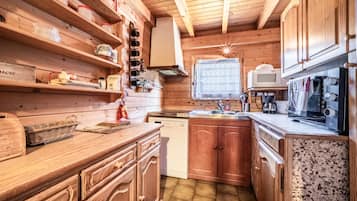 Interior de una cabaña de madera con área de cocina, armarios de madera, microondas y lavavajillas.