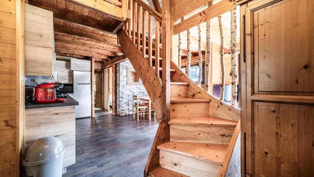 Una escalera de madera que lleva a un entrepiso con cocina y comedor.
