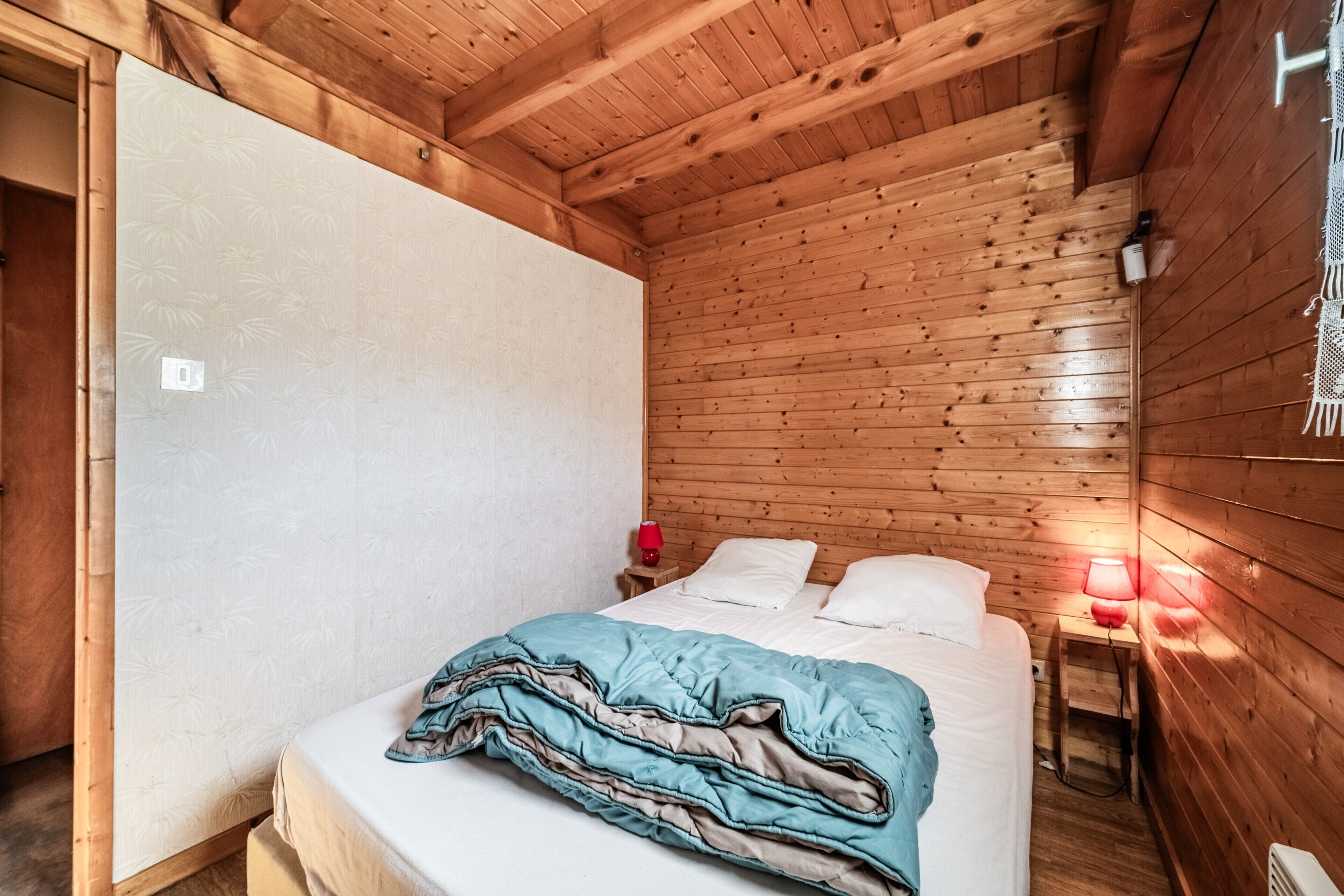 Une pièce de cabane en bois comprenant un lit, une table de chevet, une lampe rouge et un plafond en bois.