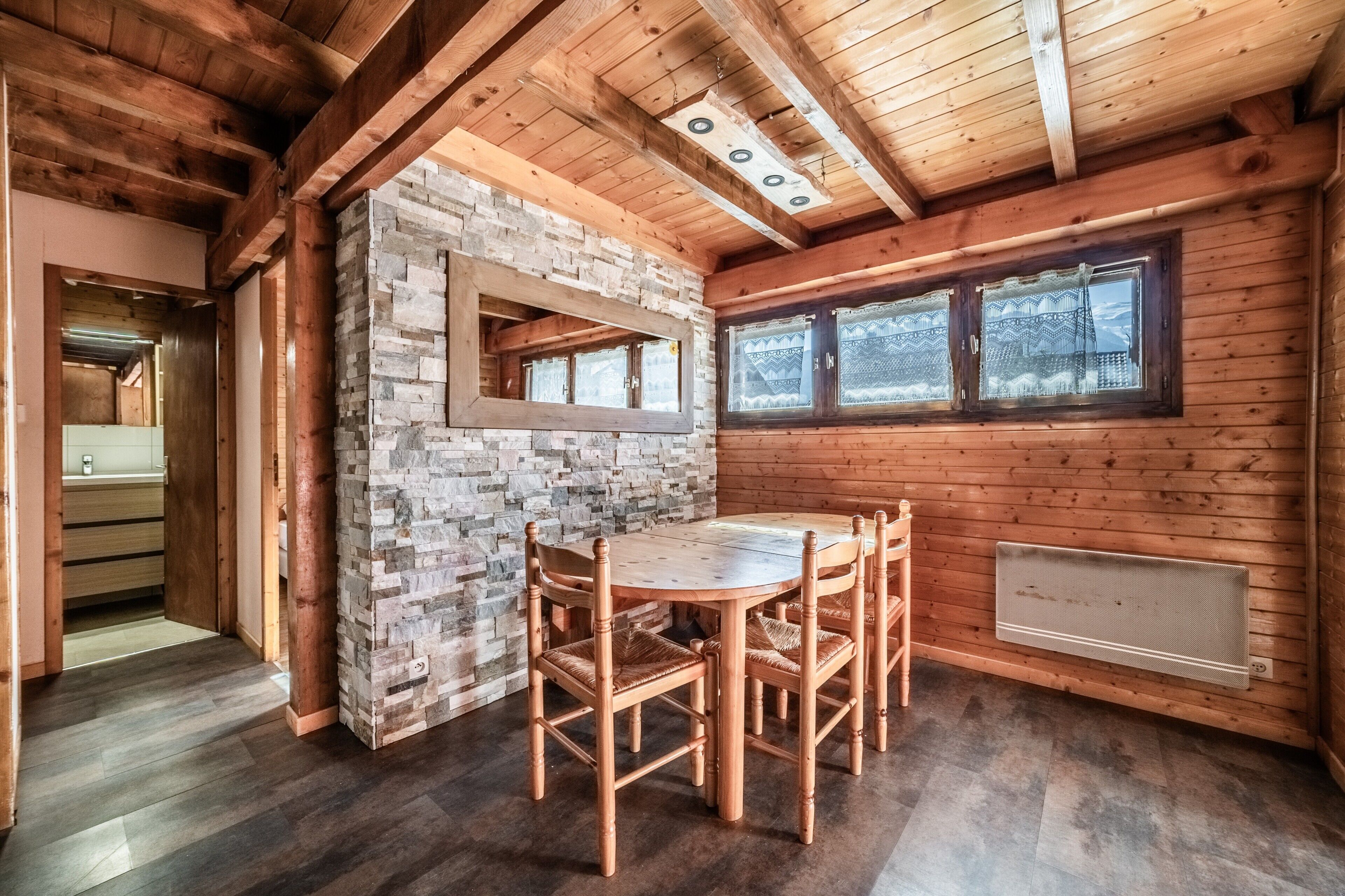 Un interior de madera con pared de piedra, una mesa redonda de madera y una ventana con cortinas estampadas.