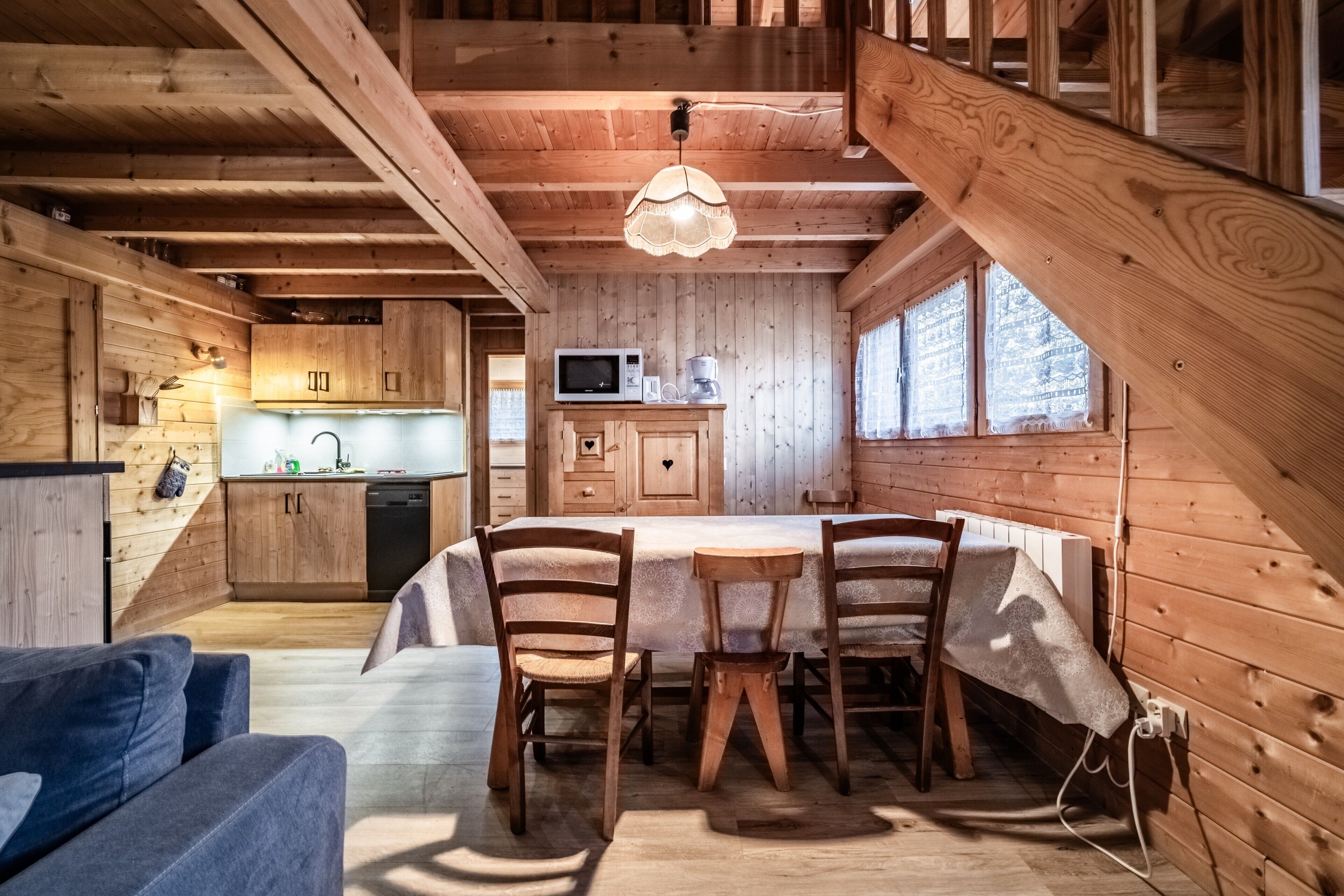 Interior de una cabaña de madera con comedor, cocina y habitación en altillo.