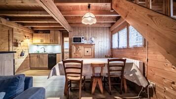 Interior de una cabaña de madera con comedor, cocina y habitación en altillo.