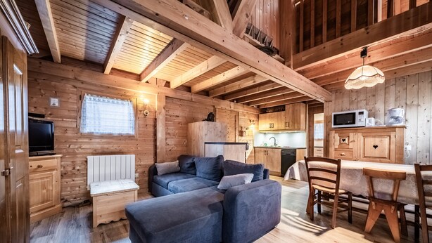 A wooden cabin interior with a sofa, dining table, and kitchen area. - Chalet “4p Comfort - Les Trolles”: Mountain View, Private Terrace & Wi-Fi (Verchaix)