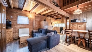 Interior de una cabaña de madera con sofá, mesa de comedor y zona de cocina.