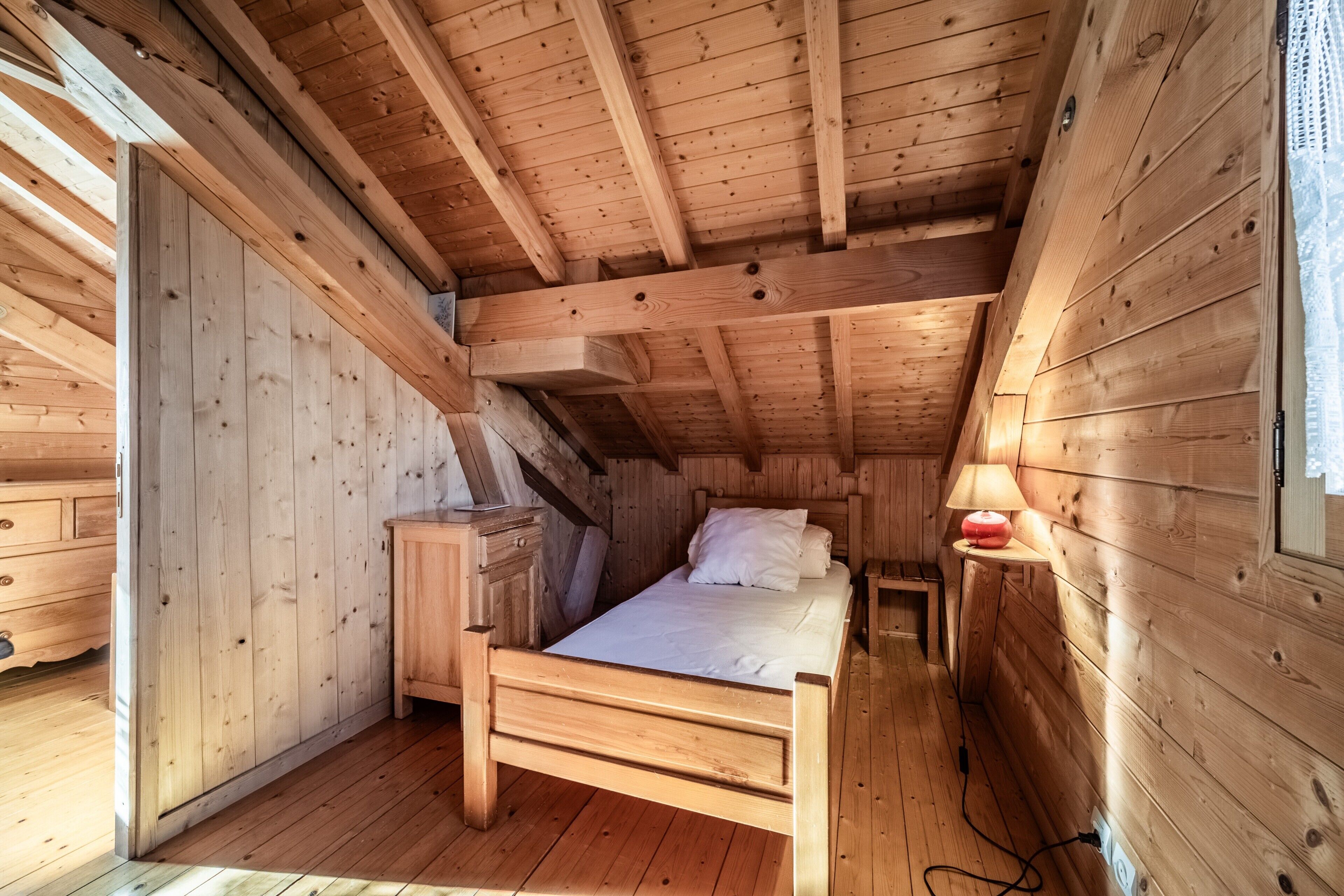 Un dormitori d'una cabana de fusta amb un llit, una tauleta de nit, una làmpada i un armari.