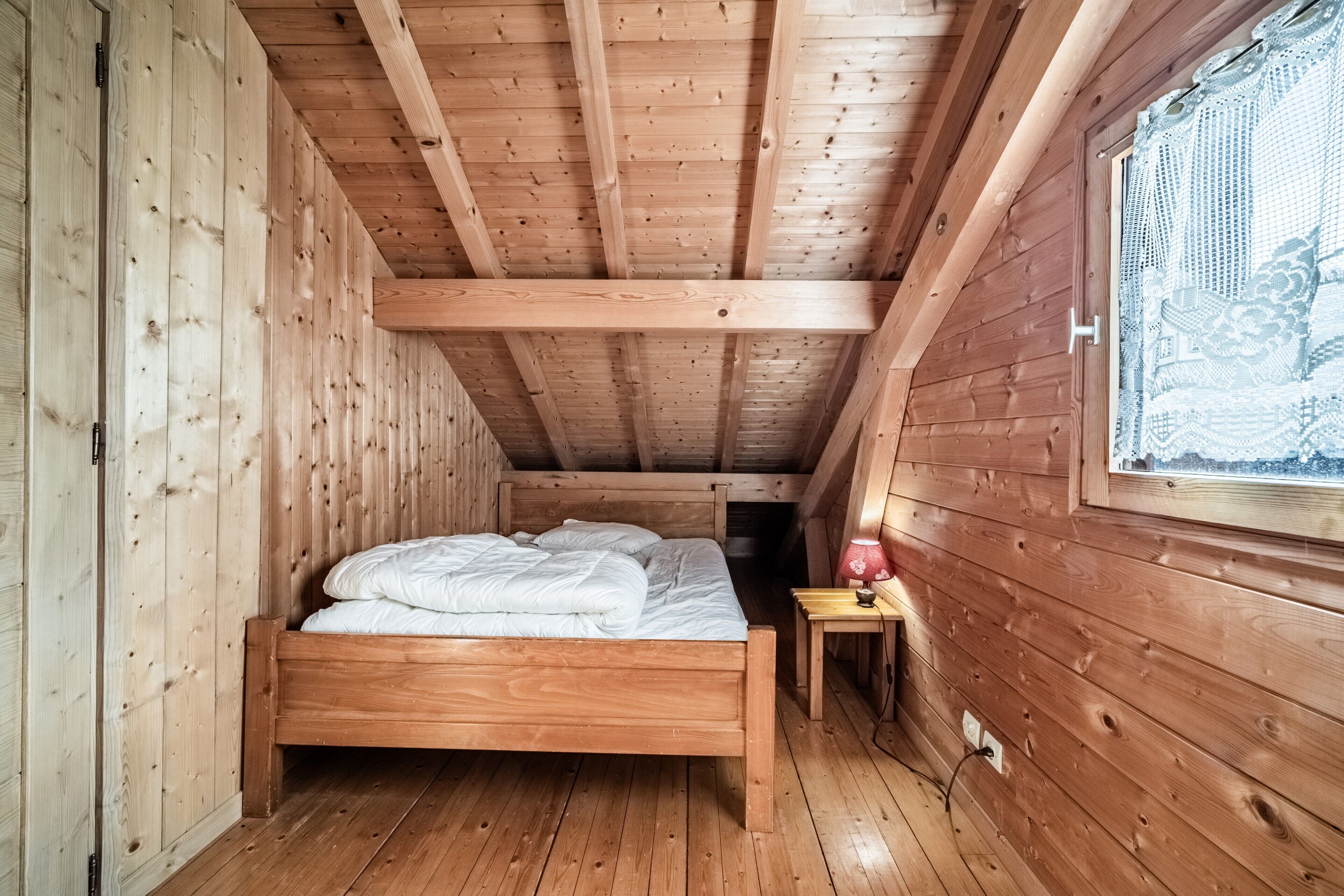 Un dormitorio de cabaña de madera con cama, mesita de noche y ventana.
