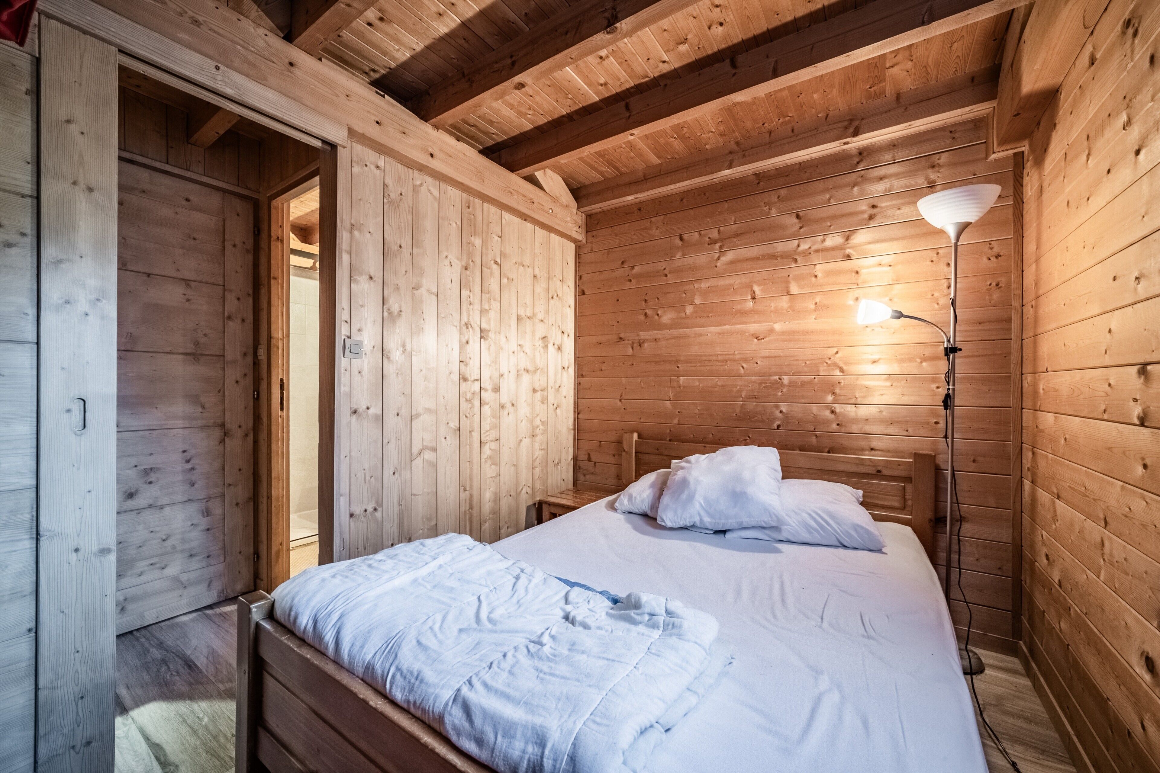 Un dormitorio de cabaña de madera con cama, lámpara de noche y armario de madera.