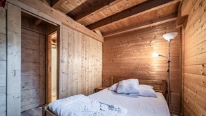 A wooden cabin bedroom with a bed, bedside lamp, and a wooden wardrobe. - Chalet “4p Comfort - Les Trolles”: Mountain View, Private Terrace & Wi-Fi (Verchaix)