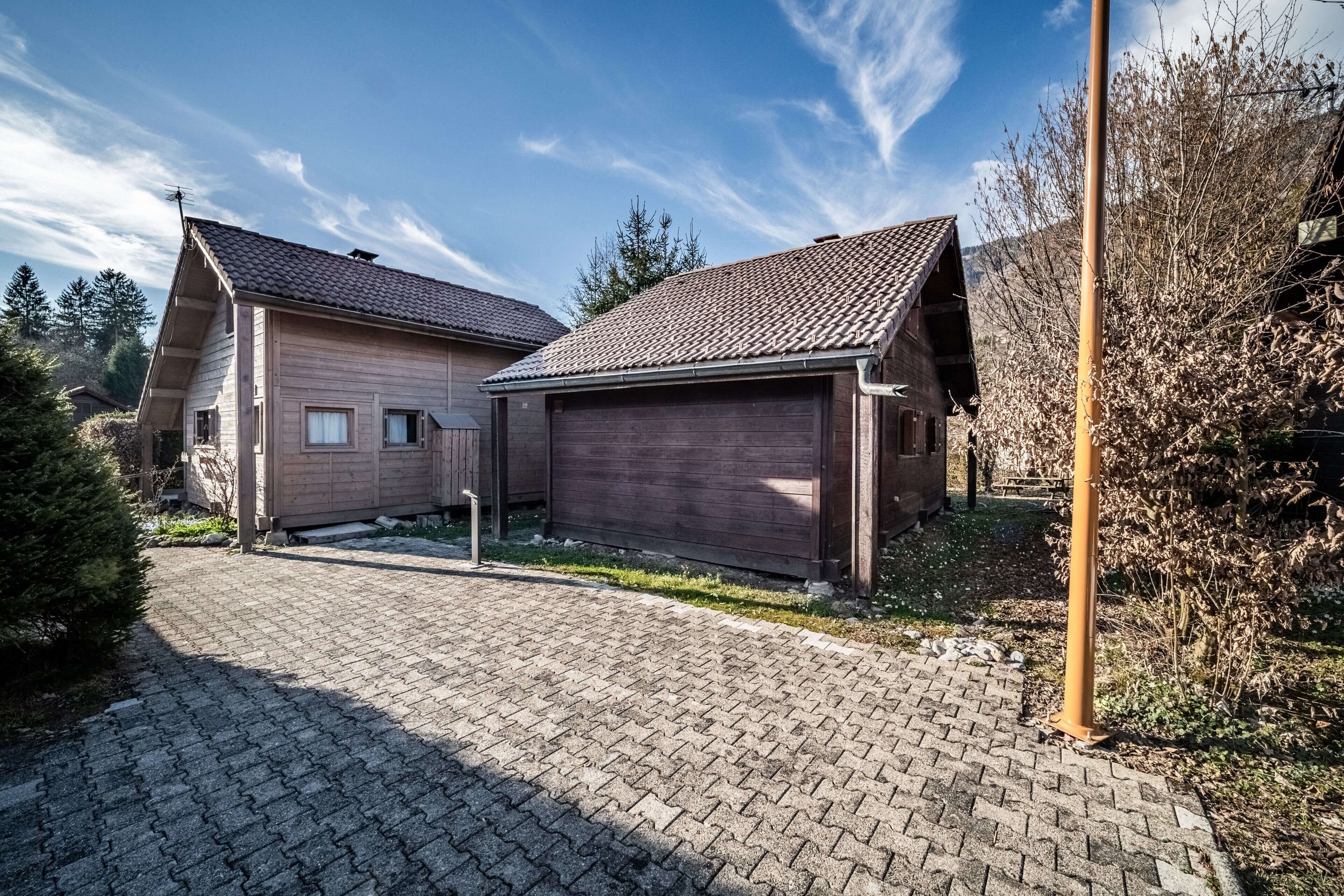 Une maison en bois à deux étages, avec un toit en tuiles, une allée pavée et une clôture en bois.
