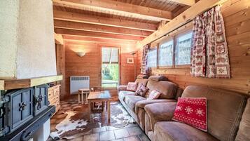 Een gezellig cabin interieur met een houten plafond, een bank met gestreepte kussens, een eettafel en een vachttapijt.