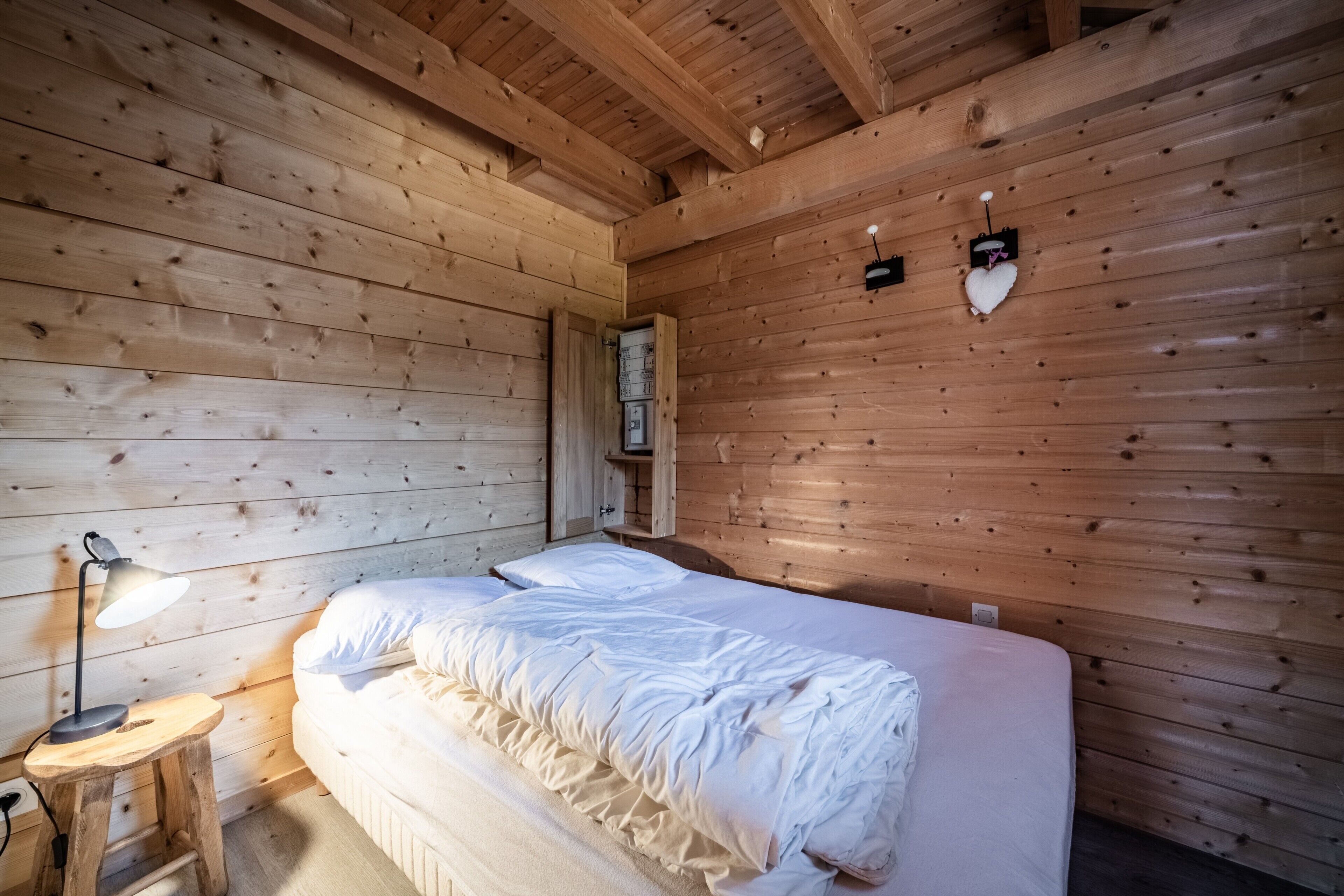 Une pièce aux murs lambrés, comprenant un lit, une table de chevet et un luminaire fixé au mur.