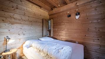Een kamer met houten lambrisering, een bed, een nachtkastje en een wandlamp.