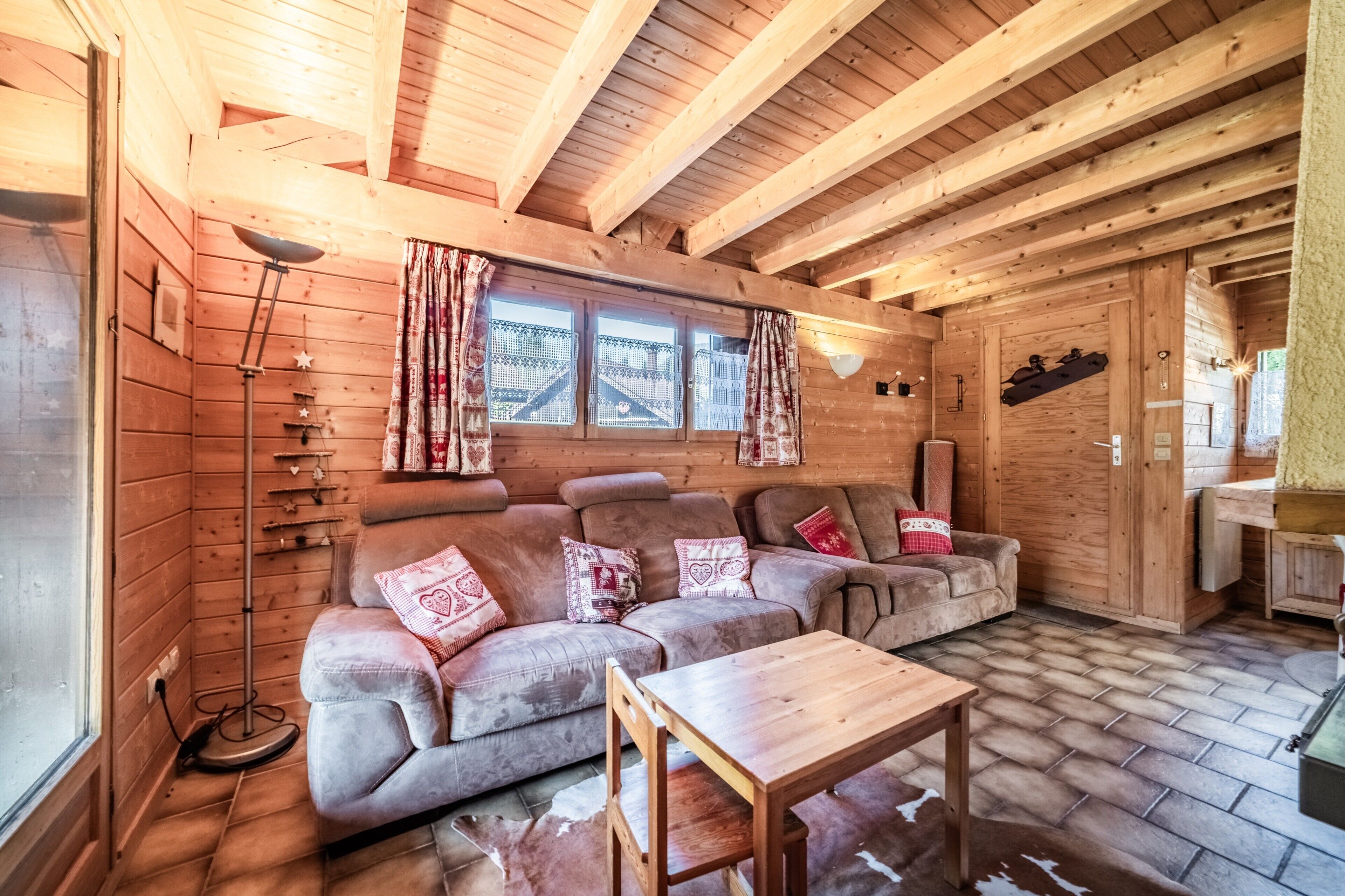 L’intérieur d’un chalet chaleureux, avec un canapé, une table et une fenêtre agrémentée de rideaux.