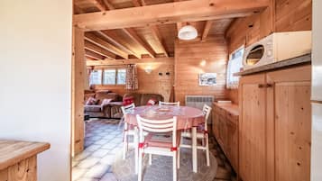 Un interior de madera con una mesa redonda de comedor, sillas, una zona de cocina y una sala de estar con sofá.