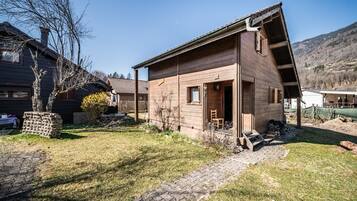 Une cabane en bois avec un toit en pente, un petit porche et un chemin en briques menant à l’entrée.