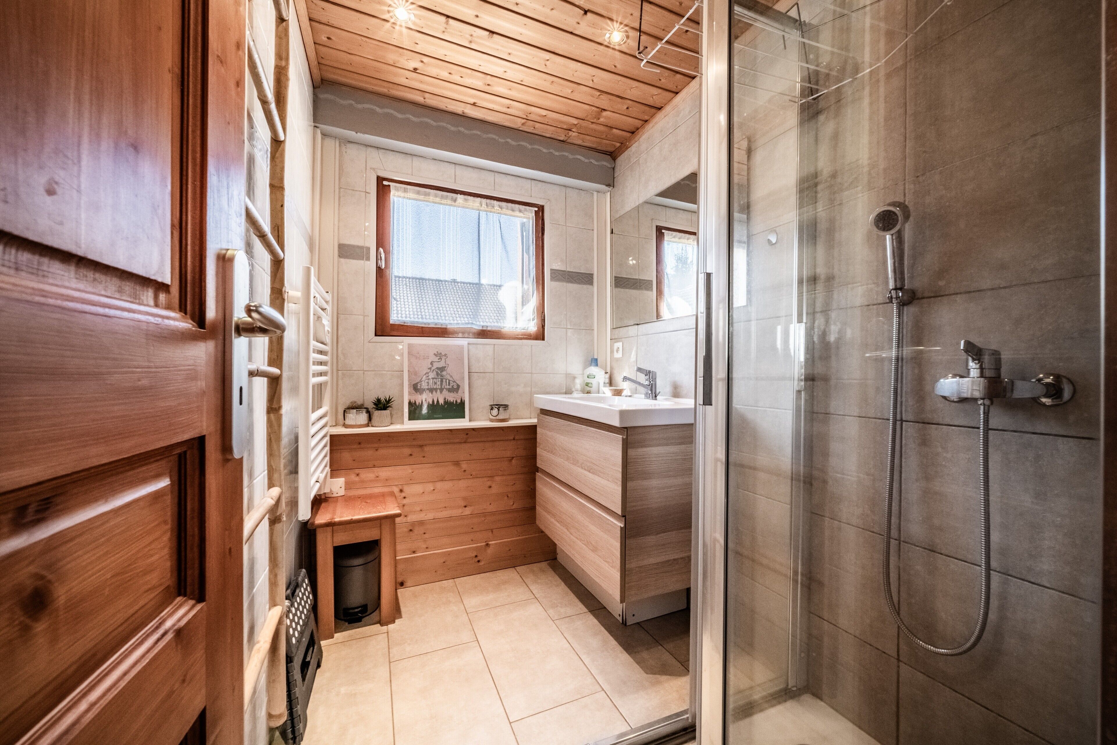 A compact bathroom with a shower, a small window, and wooden walls.