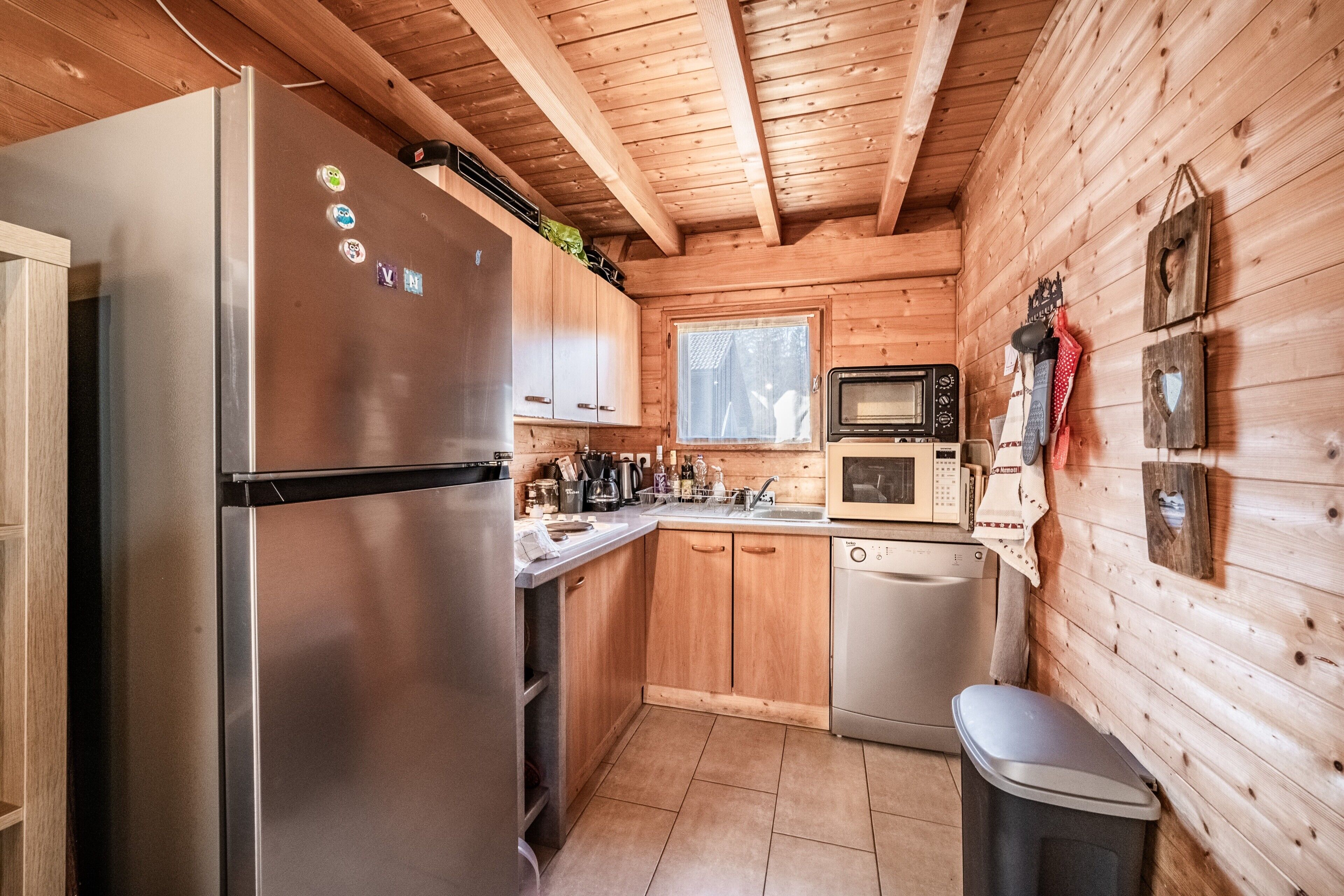Una cocina compacta con refrigerador de acero inoxidable, armarios de madera, microondas y lavavajillas.