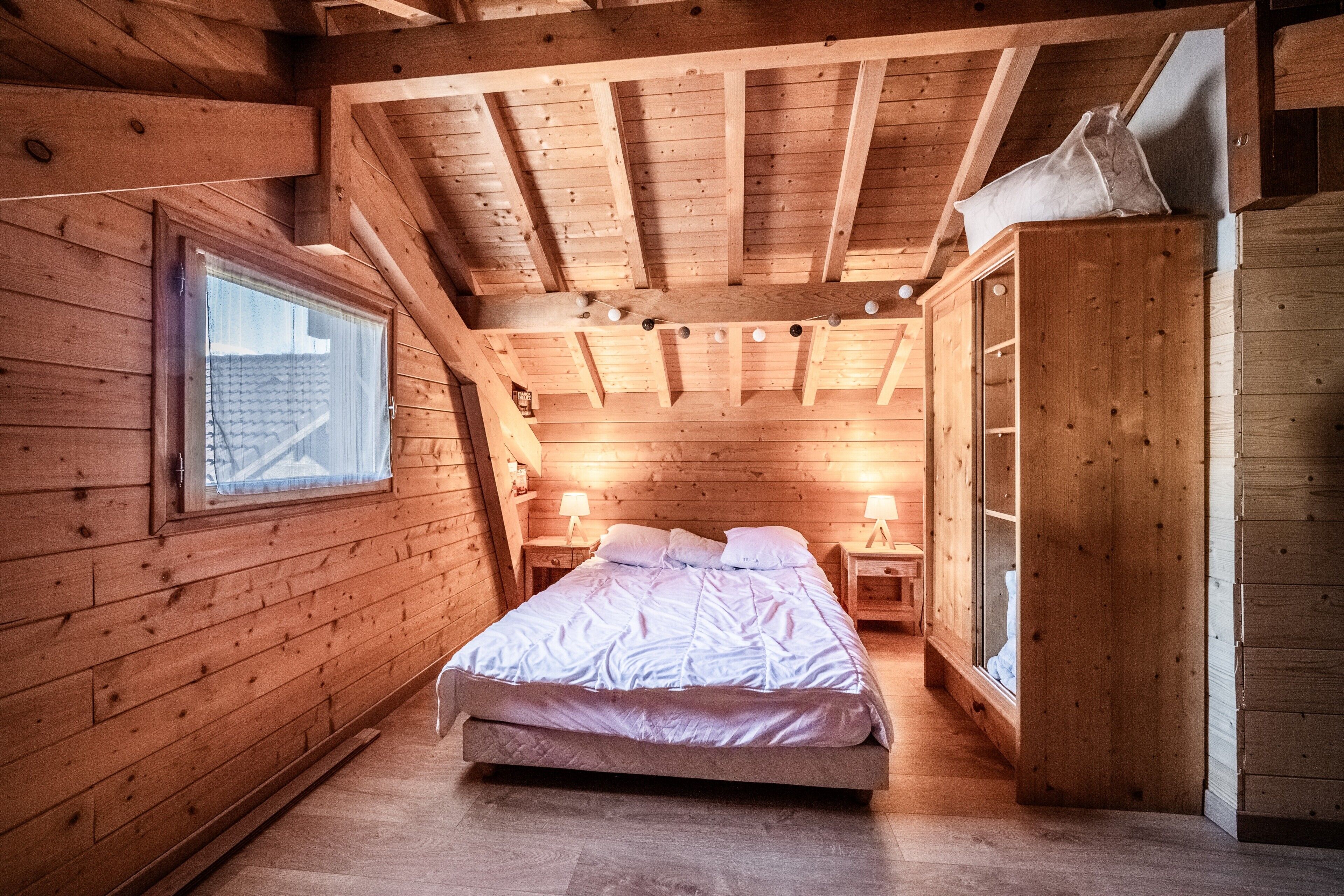 Un dormitorio de cabaña de madera con cama, mesitas de noche, un armario y una ventana.