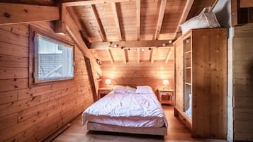 A wooden cabin bedroom with a bed, bedside tables, a wardrobe, and a window.