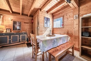 A wooden cabin interior with a dining table, chairs, a bench, a cabinet, and a fireplace. - Chalet “6p Classique - Le Rhodo” with Mountain View, Private Terrace, and Wi-Fi (Verchaix)