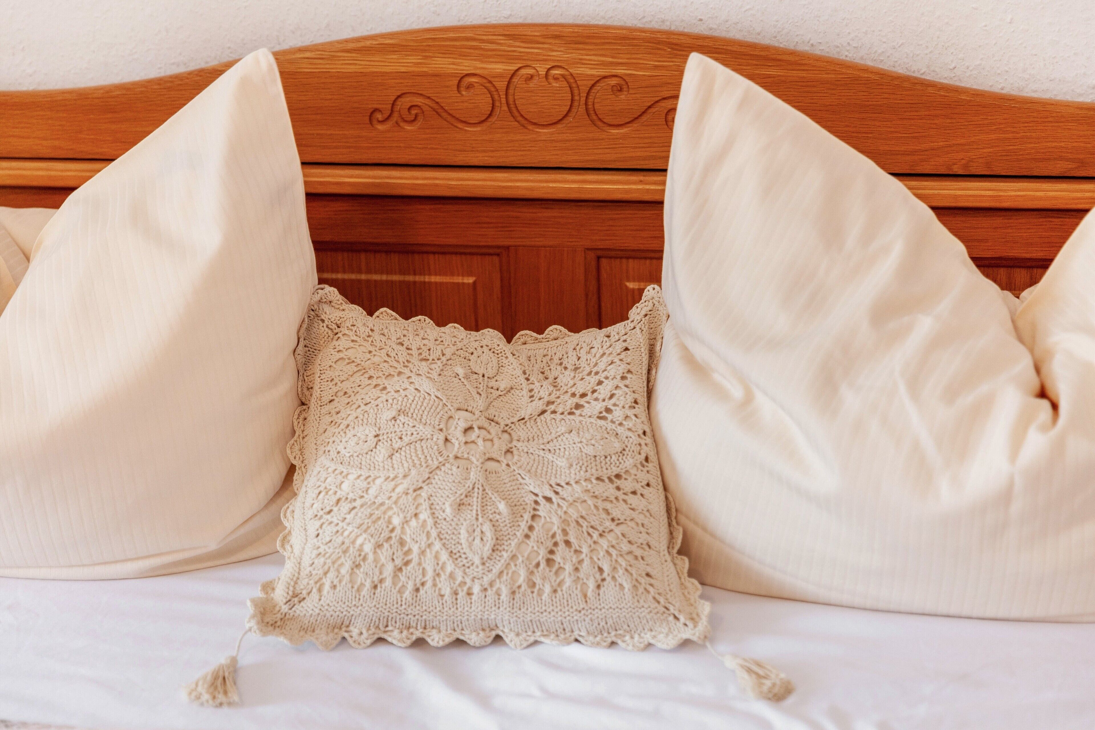 Een bed met een houten hoofdbord, twee kussens en een gebreide plaid.
