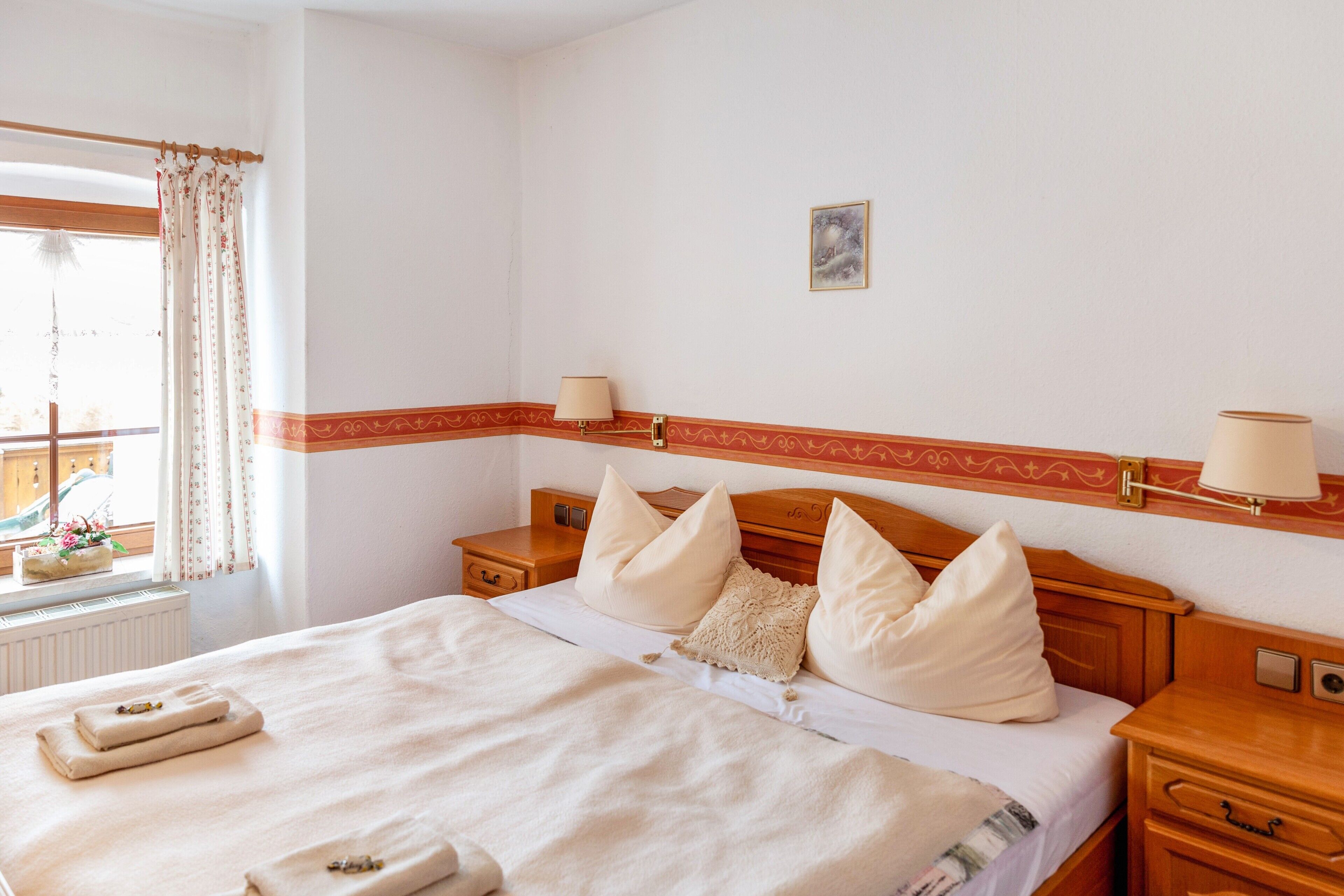 A hotel room with a bed, bedside tables, a window with curtains, and a wall-mounted lamp.