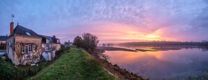 Talo rauhallisella järvellä auringonlaskun aikaan, taivaalla ei pilviä.