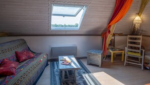 A cozy room with a sloped ceiling, a window, a sofa with patterned cushions, a small table, a chair, and a decorative lamp. - Le Balcon De Loire - Curry Room: Escape and Serenity by the Loire (La Chapelle sur Loire)