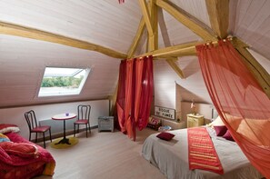 Ein Schlafzimmer mit schrägen Wänden, einem Himmelsbett, einem kleinen Tisch, zwei Stühlen und einem Fenster.