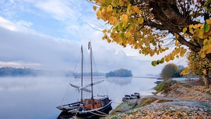 Ein ruhiger See mit Booten, einer Anlegestelle und Herbstlaub am Ufer.