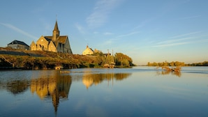 Ein ruhiger Fluss mit einer Kirche und Wohnhäusern am gegenüberliegenden Ufer.