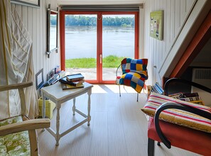 Huone, josta on näkymä järvelle, pöytä, jossa on kirjoja, värikäs tuoli ja sängyssä raidallisia tyynyjä.