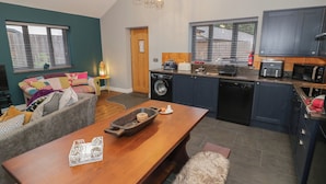 A modern kitchen with a dining area, a washing machine, and a sofa with colorful cushions. - Otter's Rest (Droitwich)