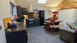 A compact kitchen with a central island, a dining area with a wooden table, and a cozy seating area with a sofa. - Otter's Rest (Droitwich)