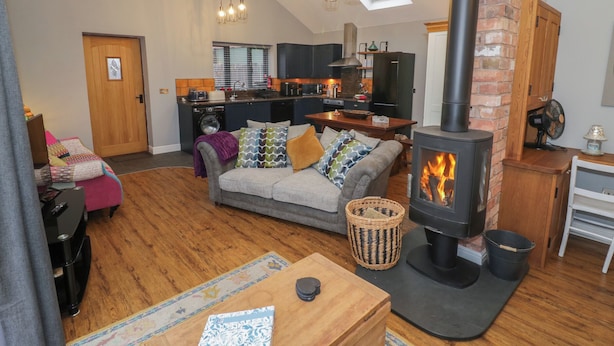 A cozy living room with a sofa, a fireplace, and a kitchen in the background. - Otter's Rest (Droitwich)