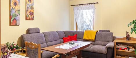 A living room with a sofa, a wooden table, a chair, a bookshelf, and two paintings on the wall.