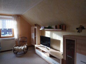 A room with a wooden entertainment unit, a television, a rocking chair, and a window with curtains.