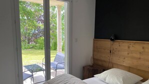 Ett sovrum med en stor säng, en sänggavel i trä och utsikt över en uteplats med stolar och ett bord.