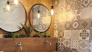 Ein modernes Badezimmer mit einem Holzwaschtisch, zwei Pendelleuchten, einem großen Spiegel und gemusterten Fliesen.