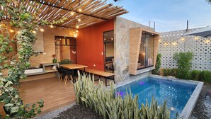 Ein moderner Poolbereich im Freien mit Holzterrasse, Sitzgelegenheiten und einer Steinwand mit geometrischem Muster.