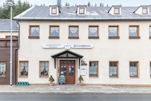 Rakennuksessa on kyltti, jossa lukee »Landgasthof & Pension» ja »Frischhütte». Siinä on perinteinen julkisivu, jossa on useita ikkunoita ja keskeinen sisäänkäynti.