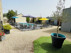 Ein Garten mit Schwimmbad, Liegestühlen und Sonnenschirmen.