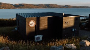 A small wooden cabin with a metal roof, a sign reading "Lapointe Ha'lets MS," and a view of a lake and hills in the background. - Lapointe Chalets - Chalet Deveau (Inverness County)