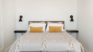 A neatly made bed with a patterned bedspread, two bedside tables with lamps, and a bench at the foot of the bed. - Lapointe Chalets - Chalet Deveau (Inverness County)
